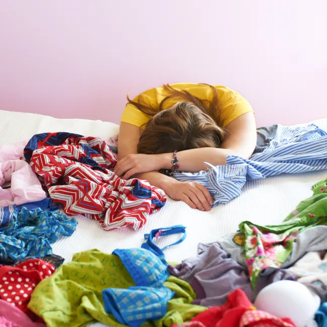 photo of a young woman frustrated with clothes all over bed
