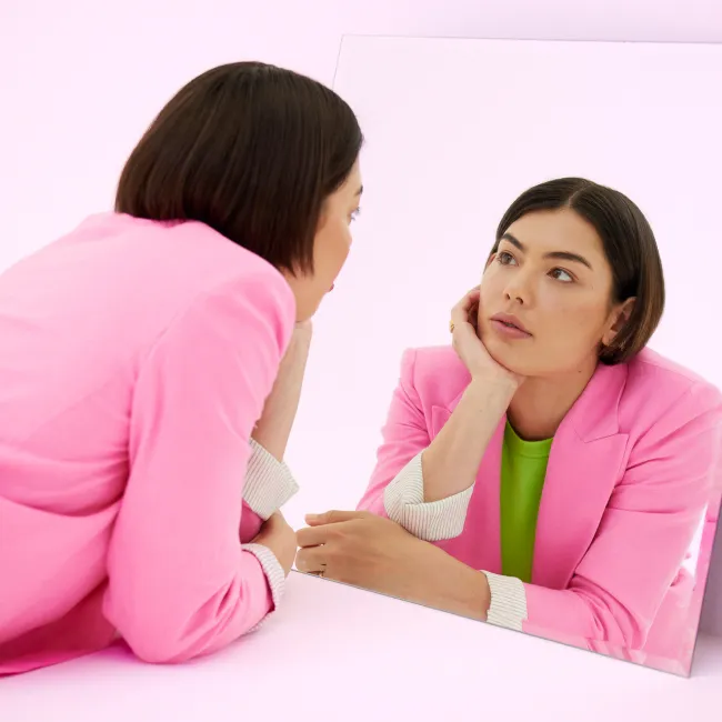 photo of woman looking at her reflection in mirror
