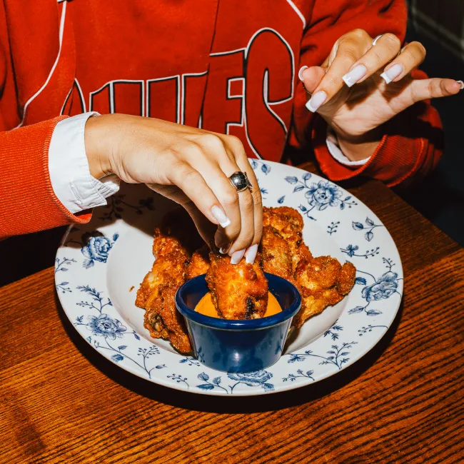 photo of a woman in a red sweater dipping a crispy fried chicken wing into sauce