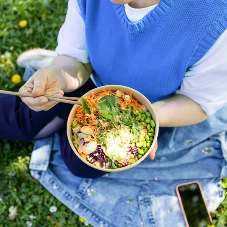 photo of a woman eating a vegetable bowl outside in a  park