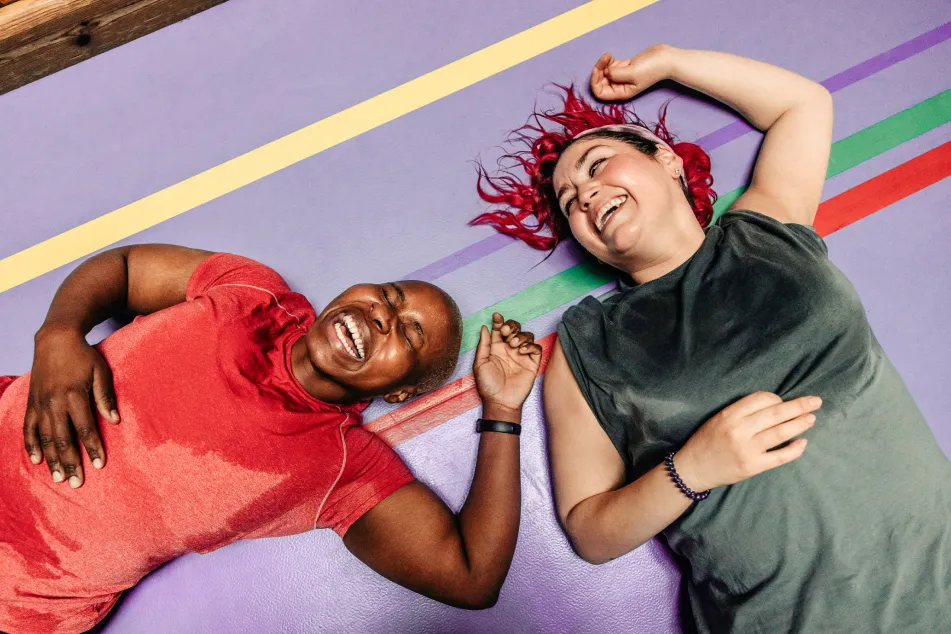 photo of female athletes laughing while lying on safety mat at sports court