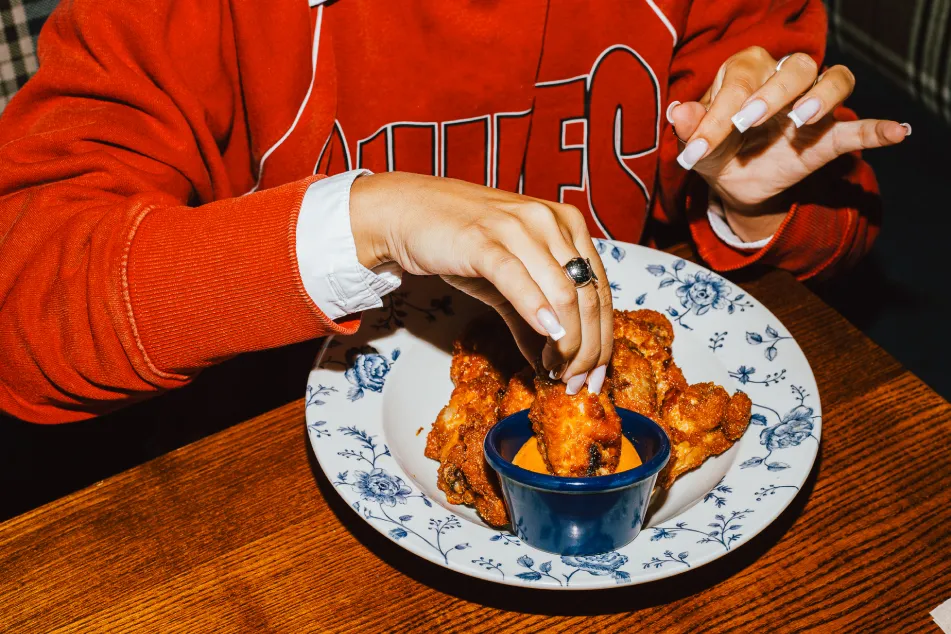 photo of a woman in a red sweater dipping a crispy fried chicken wing into sauce