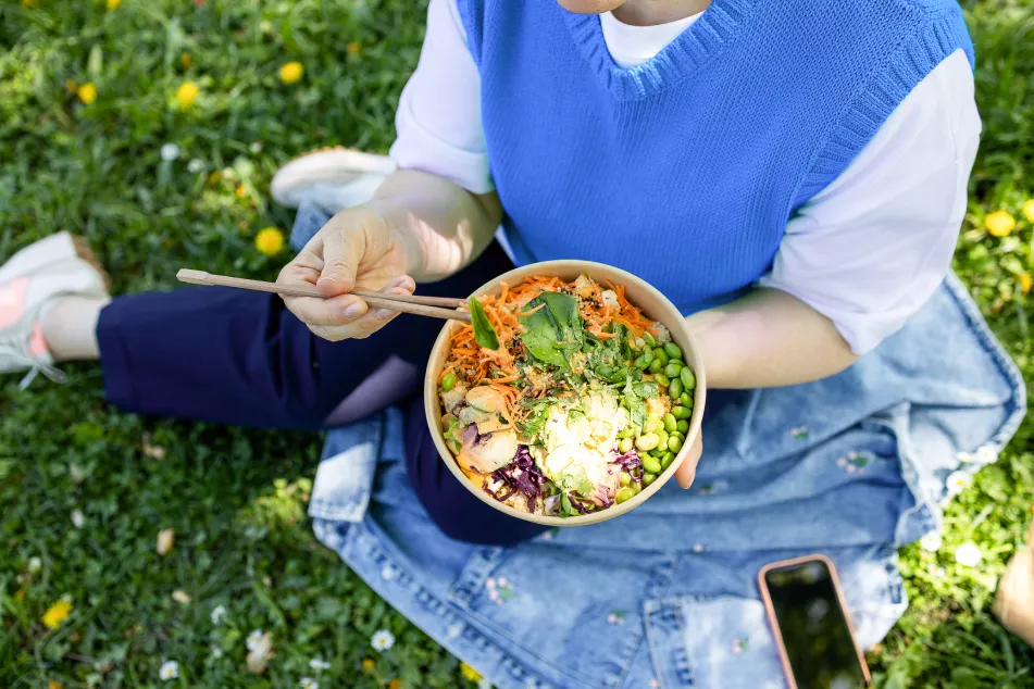 photo of a woman eating a vegetable bowl outside in a park