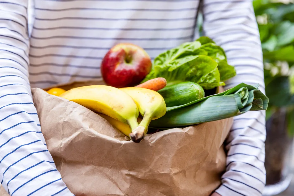 Close up of person carrying a paper bag full of fruits and vegetables