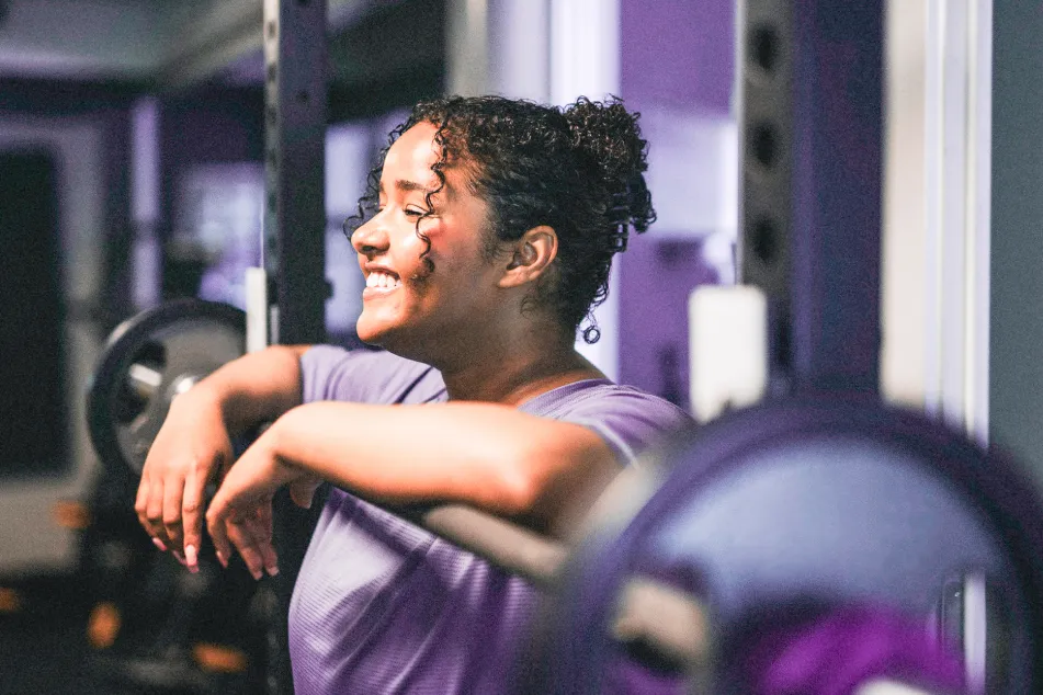 photo of a smiling young woman leaning on barbell at health club