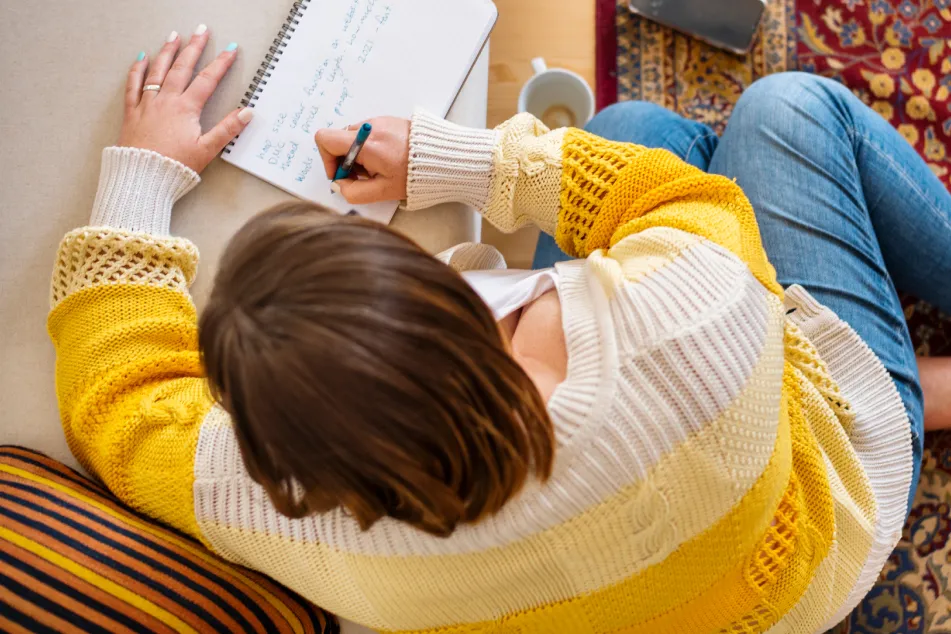 photo of a woman writing in a note pad while sitting on her living floor