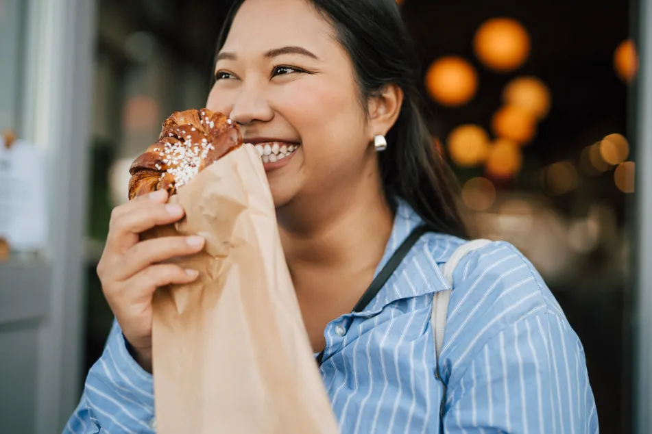 photo of a happy young woman holding fresh cinnamon bun