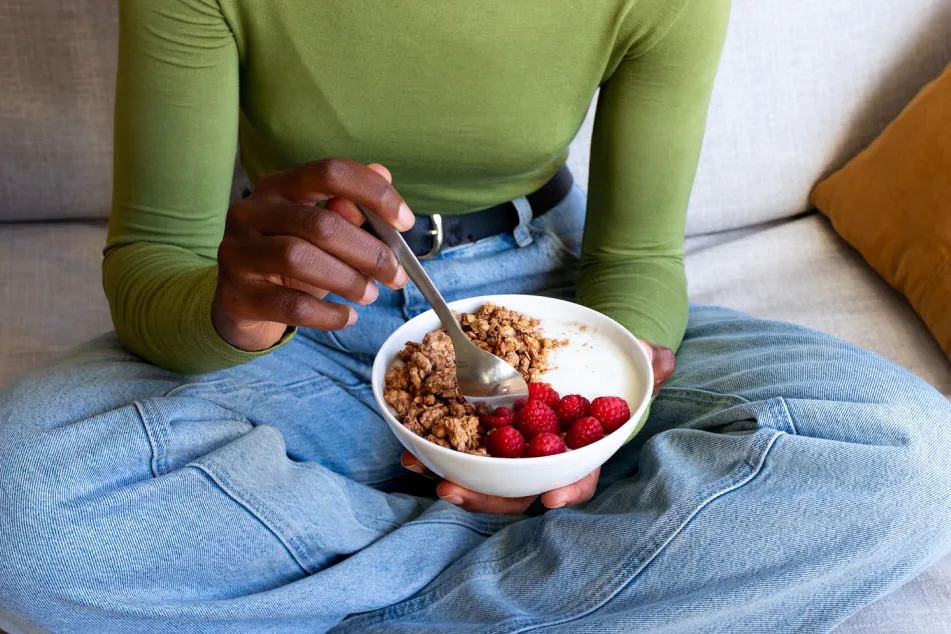 photo of a young adult woman eating granola with yogurt and raspberries