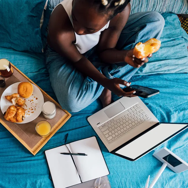 photo of a woman holding mobile phone having breakfast with girlfriend on bed