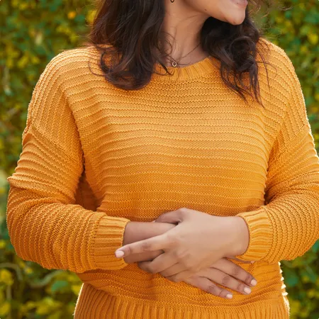 photo of a beautiful happy woman standing in front of leafy wall with hands on stomach