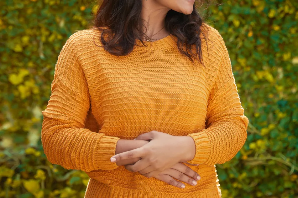 photo of a beautiful happy woman standing in front of leafy wall with hands on stomach