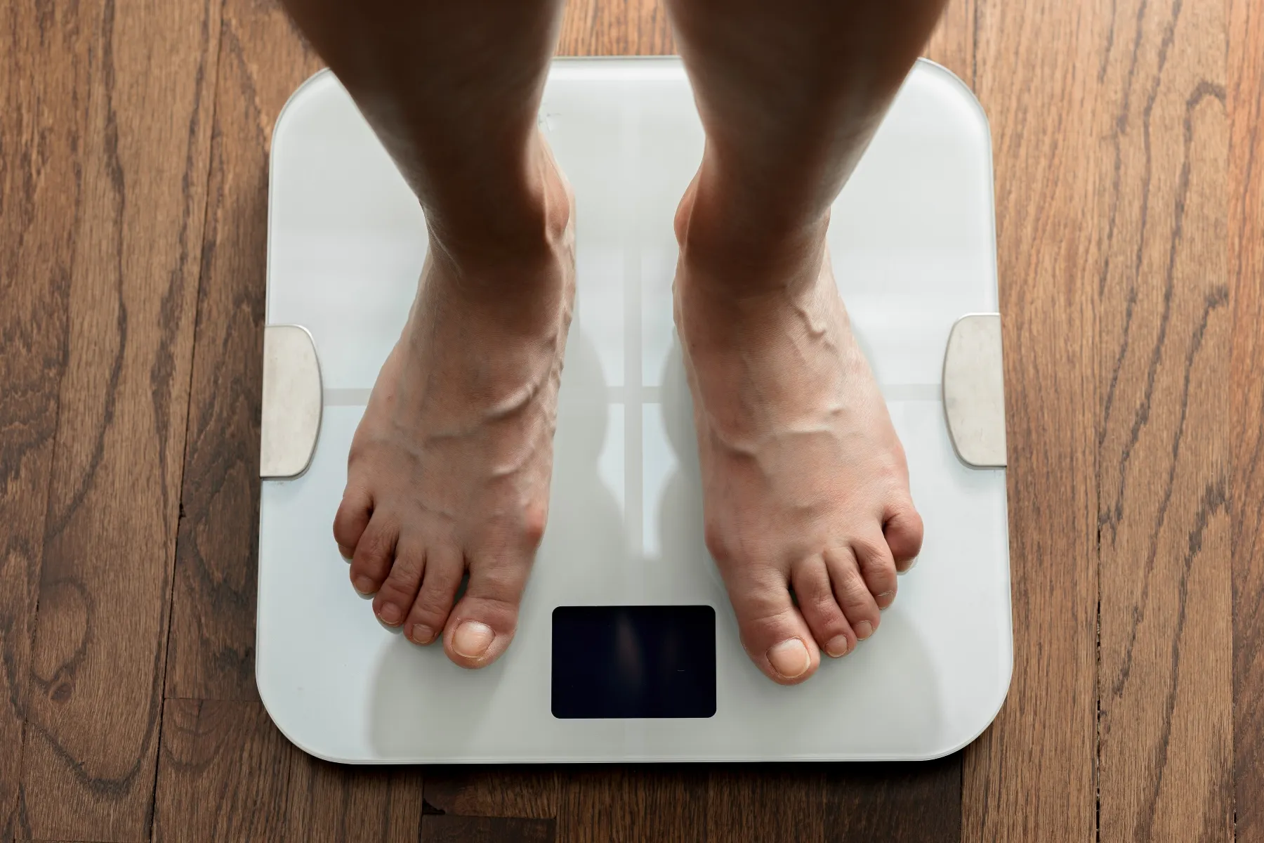 photo of feet standing on white digital bathroom scale over wooden floor
