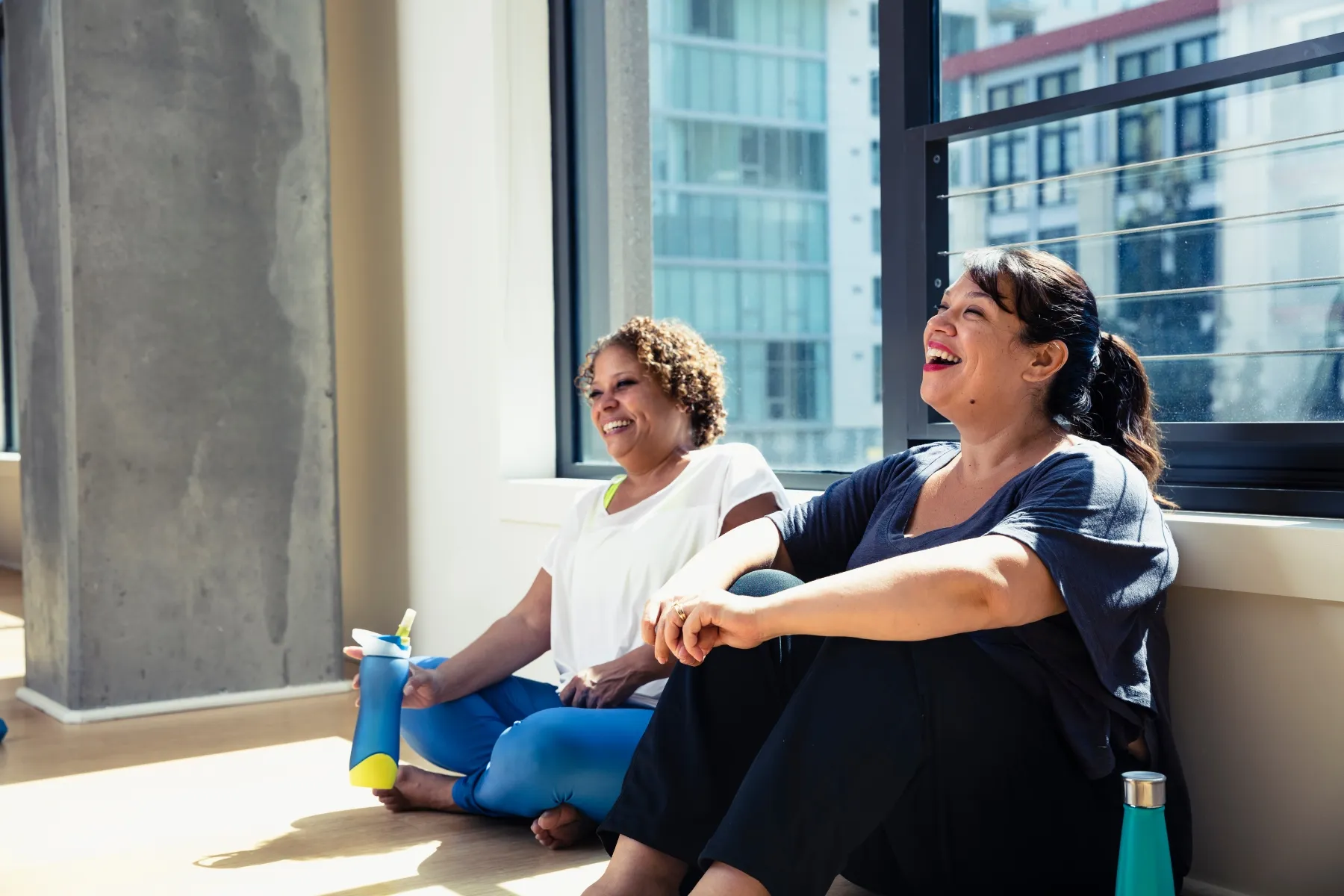 photo of female friends sitting against window in yoga studio