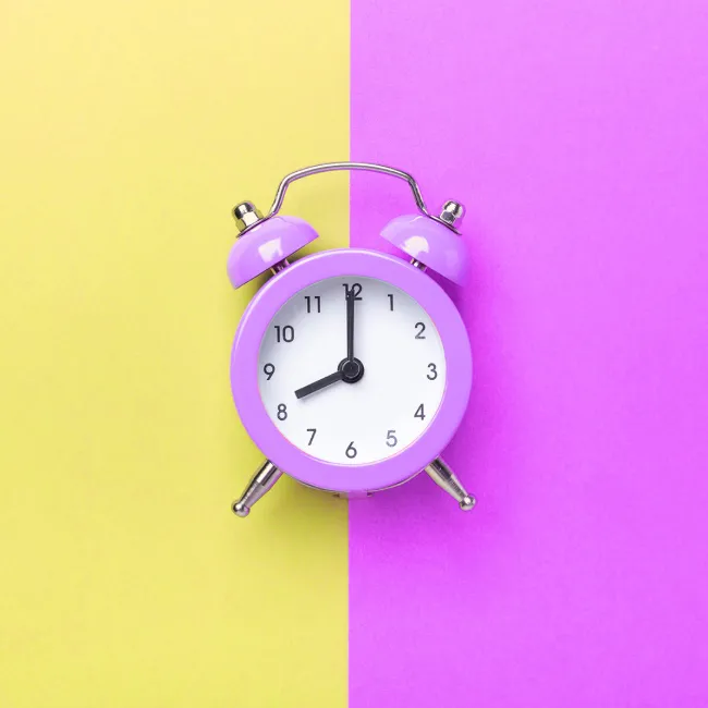 photo of purple alarm clock on two tone color purple and yellow background