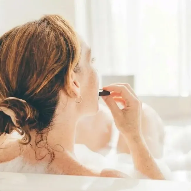 photo of woman applying serum to skin while soaking in bath