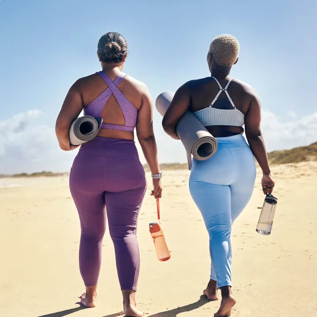 photo of women walking on beach with yoga mats