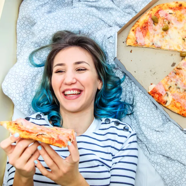photo of woman eating pizza in bed