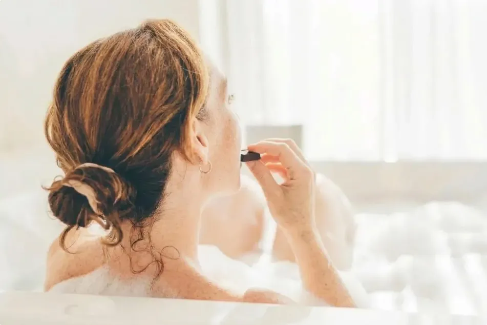 photo of woman applying serum to skin while soaking in bath