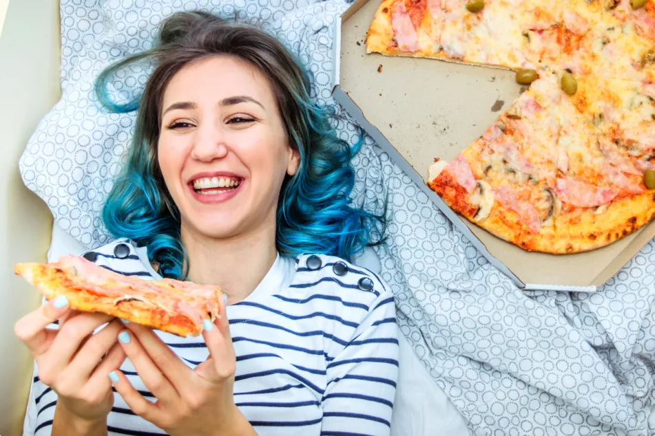 photo of woman eating pizza in bed